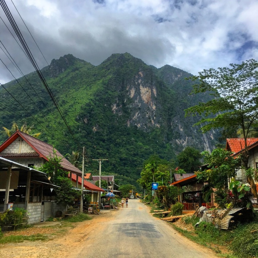 Quaint town of Nong Khiaw with buildings scattered along the road, power lines ahead, and enormous limestone mountains